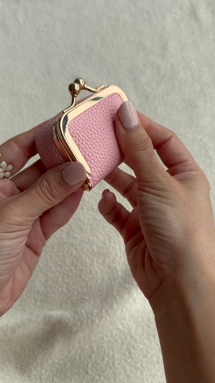 Small pink textured jewelry case with gold clasp held by two hands.