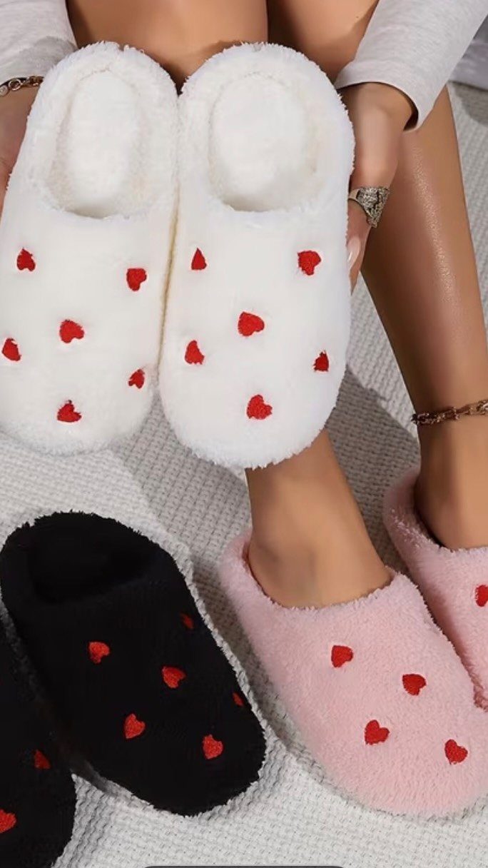 Fuzzy heart-patterned slippers in white, pink, and black on a white surface.
