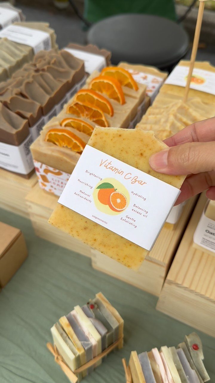 Hand holding a Vitamin C soap bar among various artisanal handmade soaps.