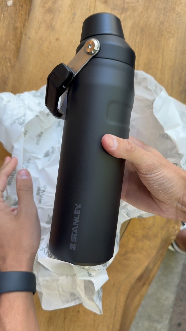 Matte black Stanley insulated water bottle held over white tissue paper on wood.