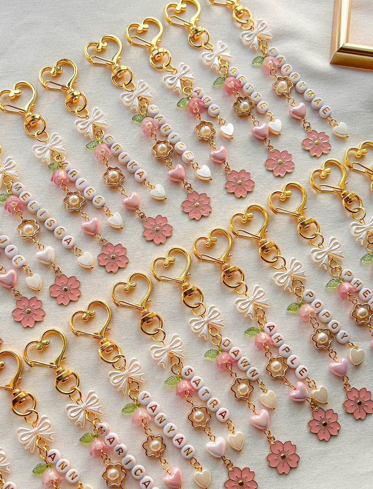Personalized beaded keychains with gold heart clasps and pink floral accents on white fabric