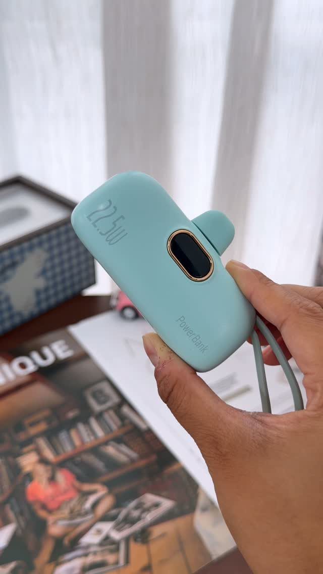 Light blue portable power bank held in a hand over a magazine.