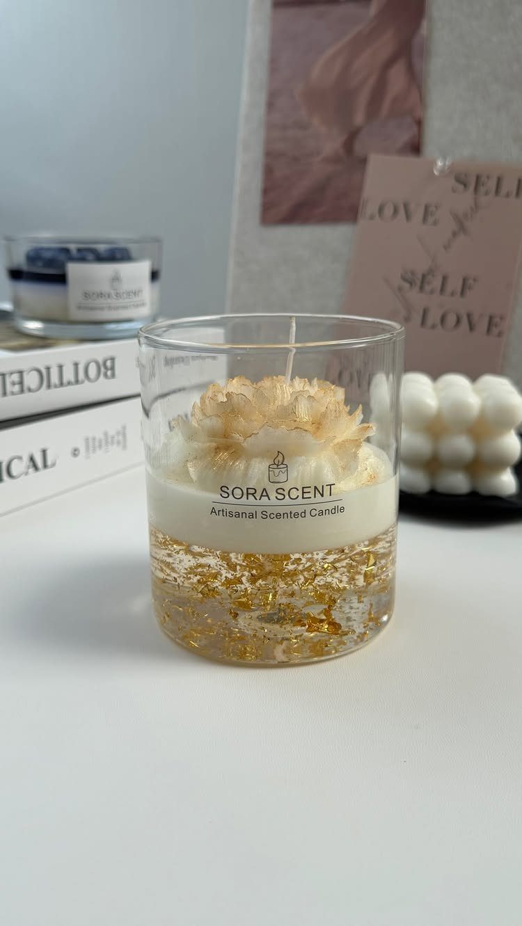 Scented candle in a glass jar with a wax flower and gold flakes.