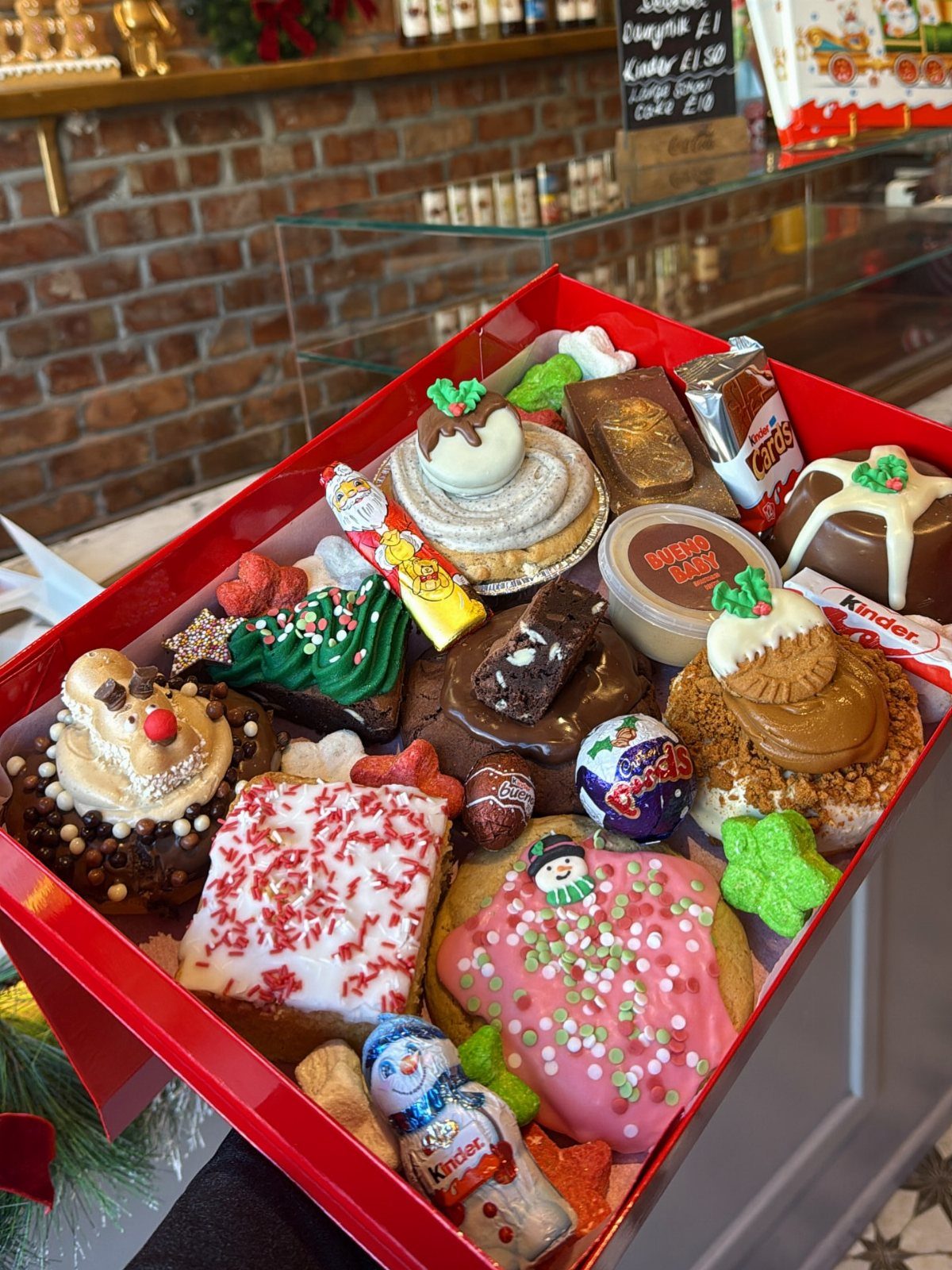 Assorted decorated cookies and chocolates arranged in a red gift bakery box.