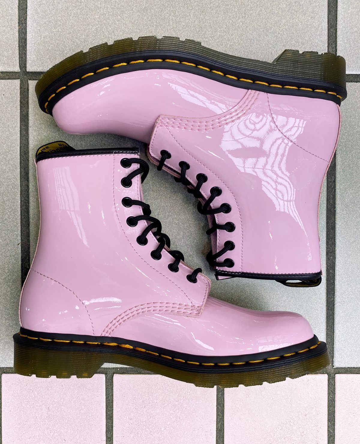 Pink patent leather lace-up boots with black laces on a grey tiled floor.