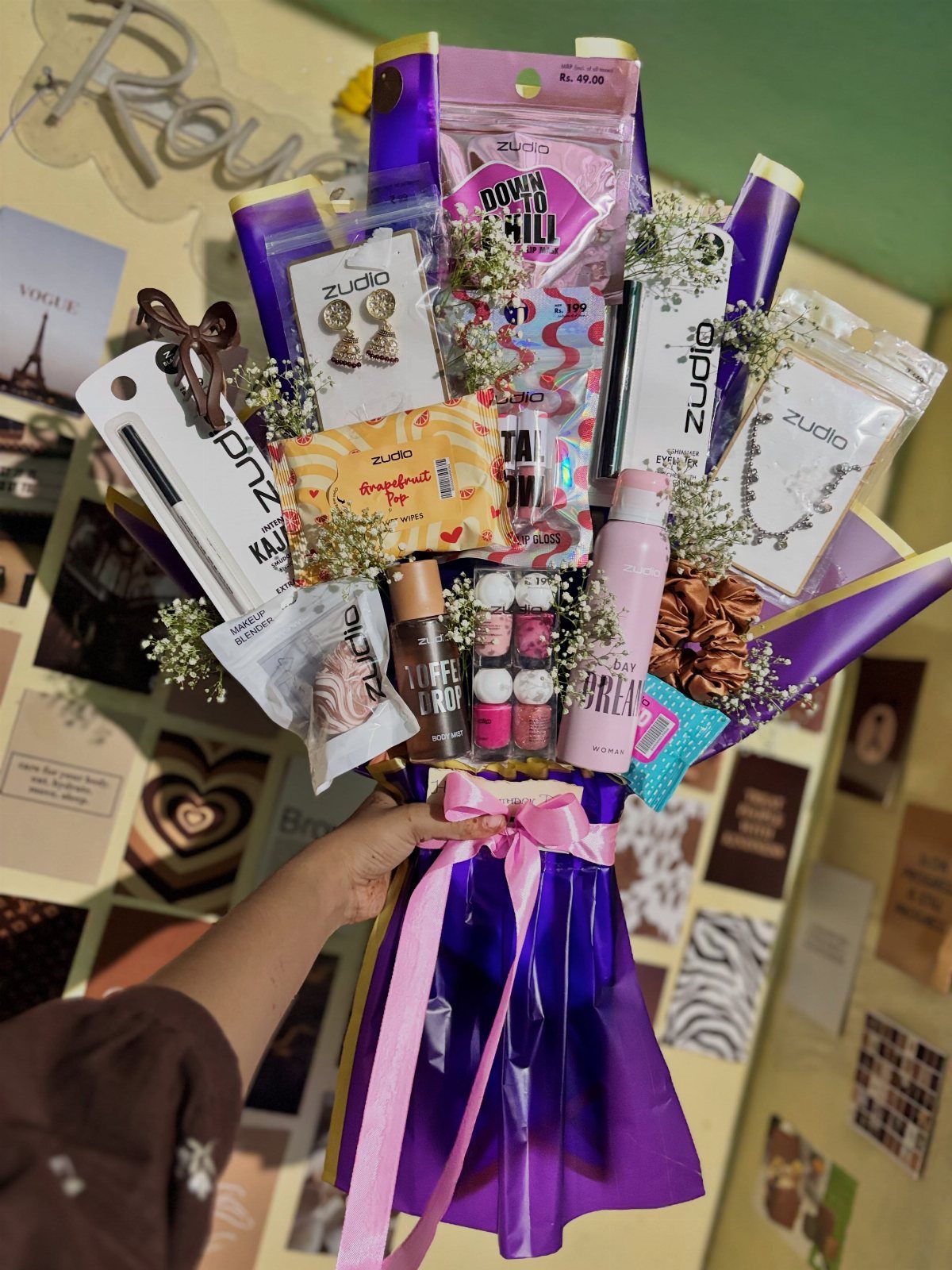 Gift bouquet wrapped in purple cellophane containing jewelry, makeup, and small white flowers.