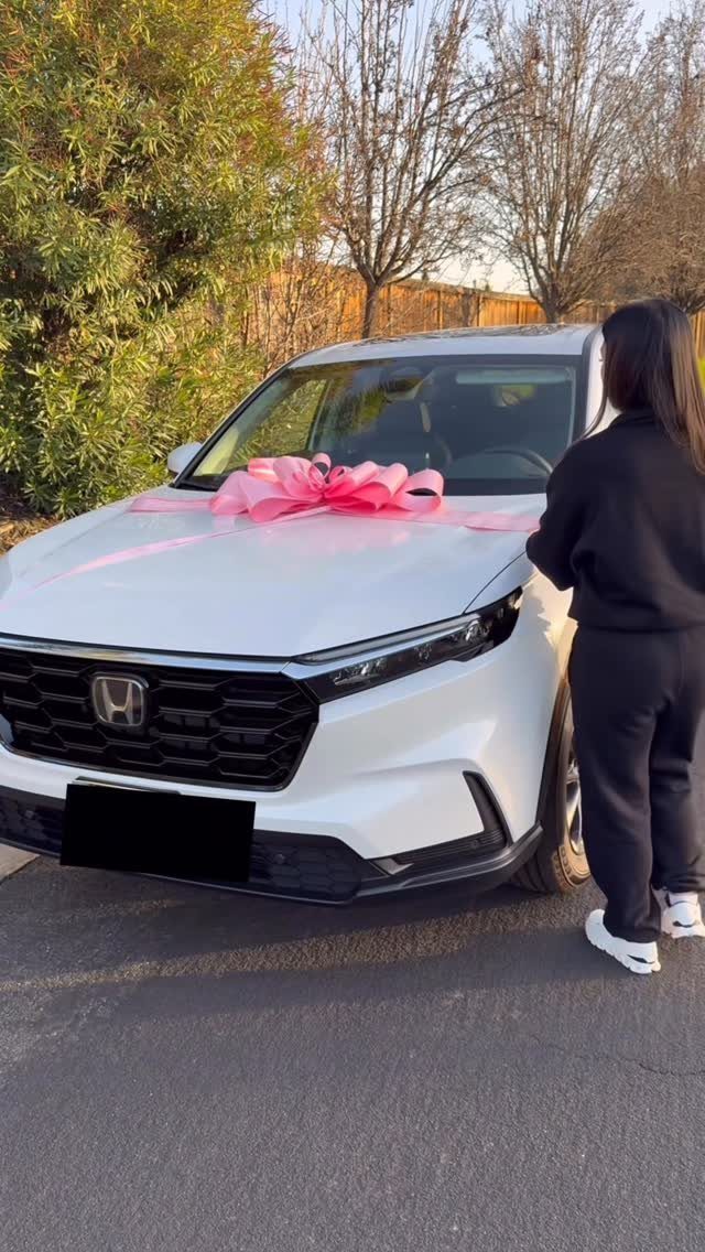White Honda SUV with a large pink bow on the hood and a person.