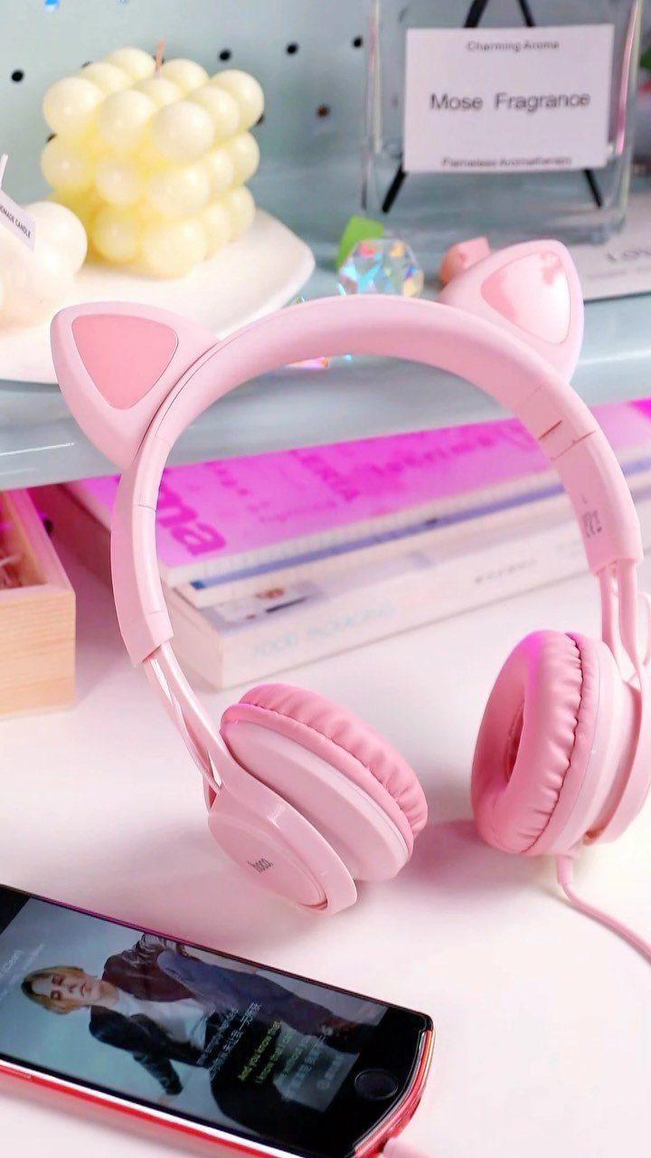 Pink cat-ear headphones on a white desk with a bubble candle and smartphone.