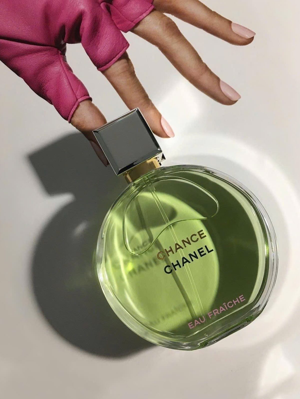 Chanel Chance Eau Fraîche perfume bottle next to a hand in pink glove