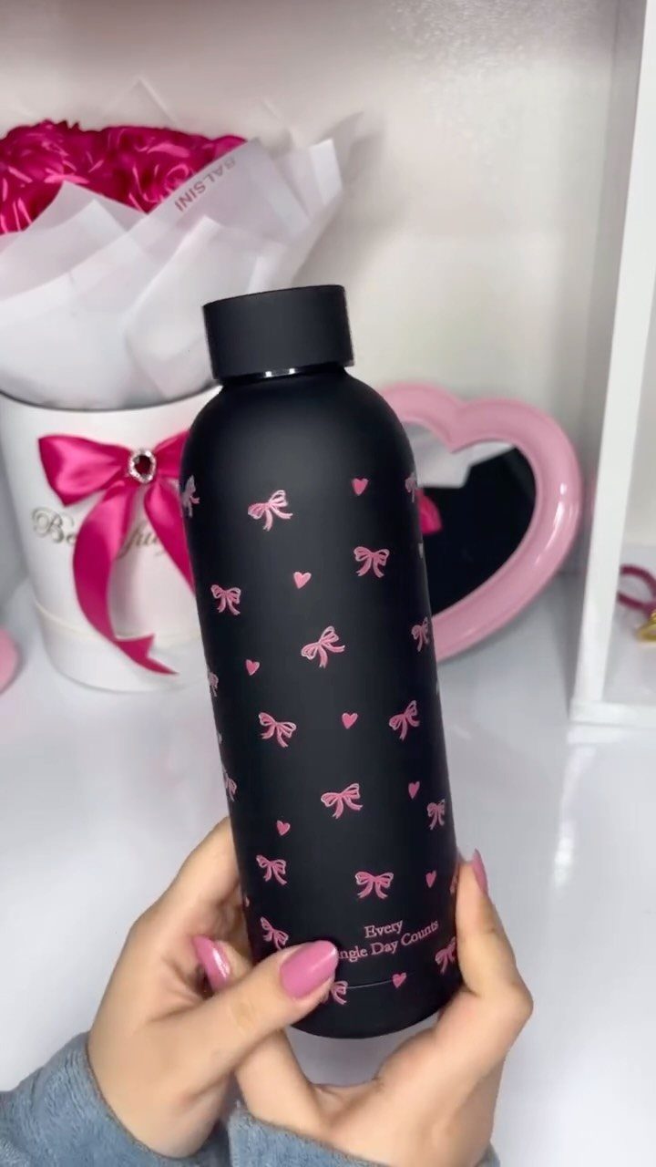 Matte black water bottle with pink bows and hearts held by a person.