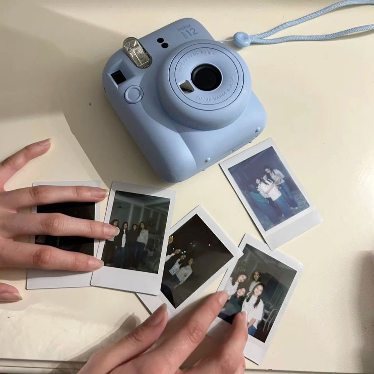 Light blue instant camera surrounded by printed polaroid photos on a white surface.