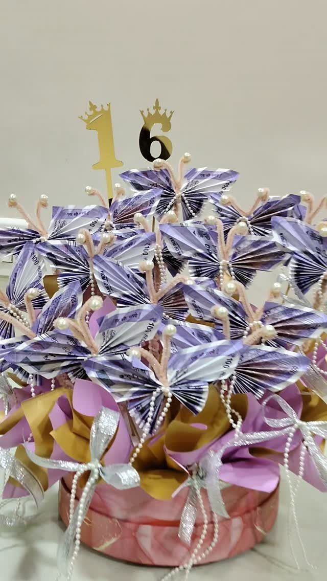 Money butterflies arrangement with a gold 16 topper in a pink marbled box