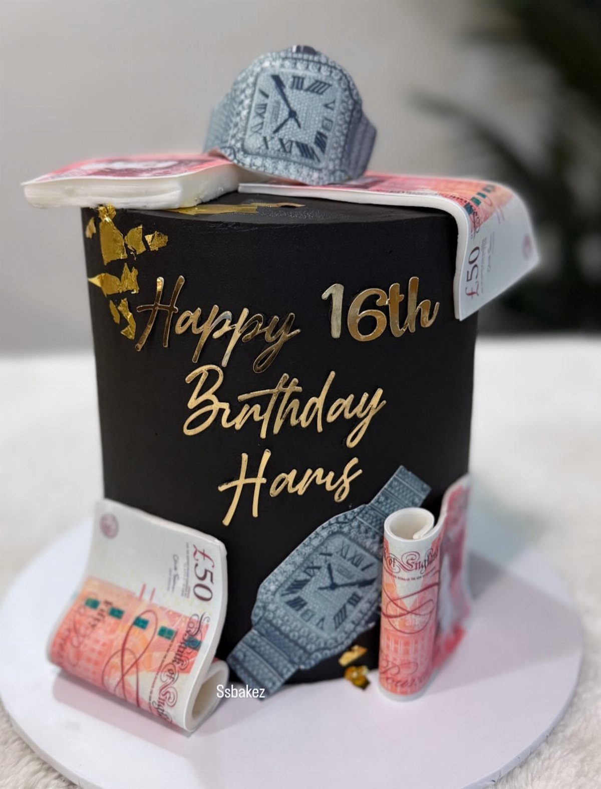 Black 16th birthday cake decorated with rolled fifty-pound notes and silver watches.