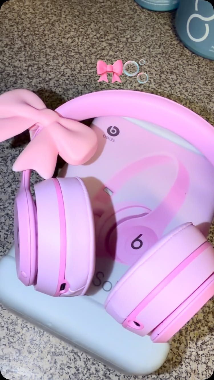 Pink over-ear headphones with a large pink bow on a white surface.