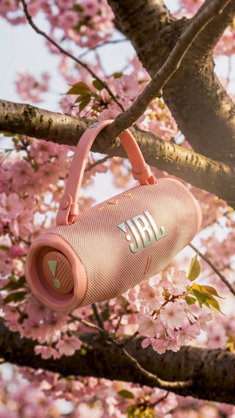 Pink JBL portable speaker hanging from a cherry blossom tree branch with flowers.
