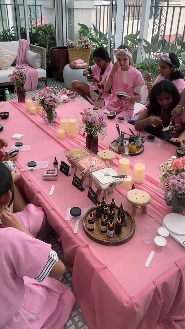 Young women in pink robes enjoying a spa day with skincare products and flowers.