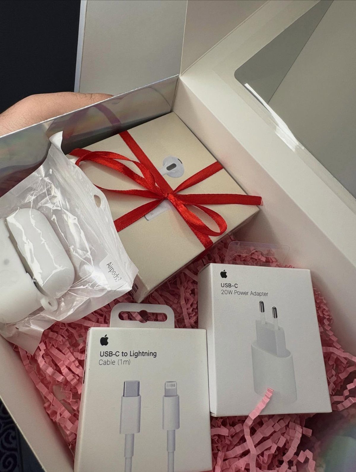 Apple AirPods and charging accessories arranged in a gift box with pink filler.