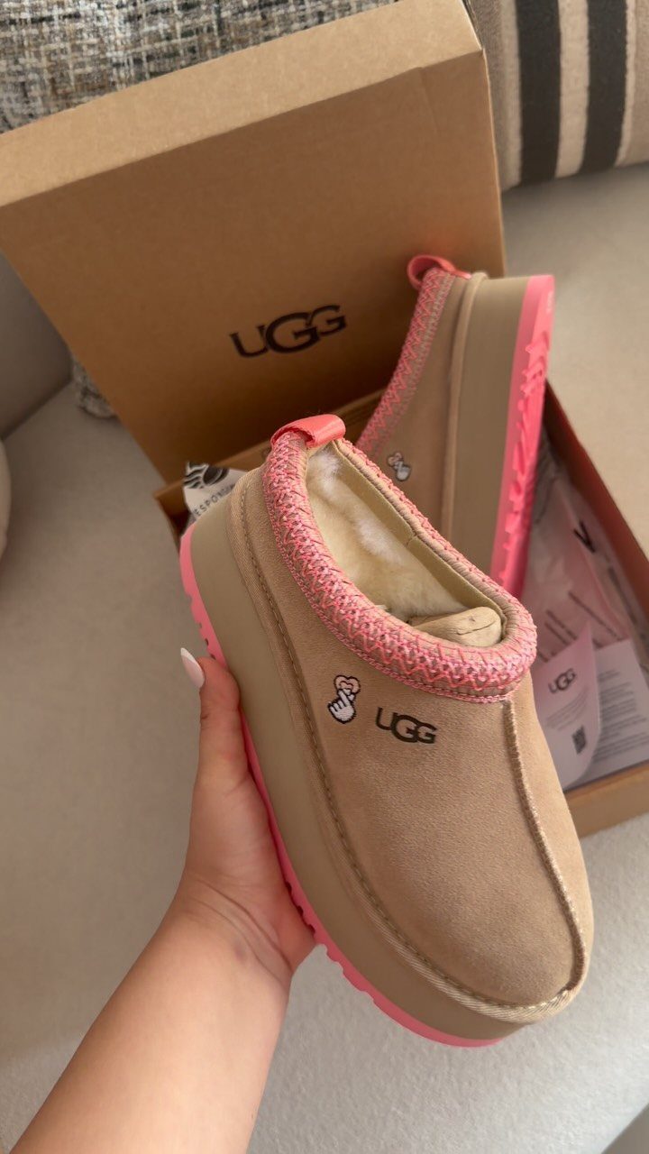 Tan suede UGG slippers with pink soles and trim next to their box.