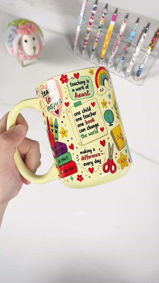 Yellow ceramic mug with teacher-themed illustrations and quotes held by a hand.