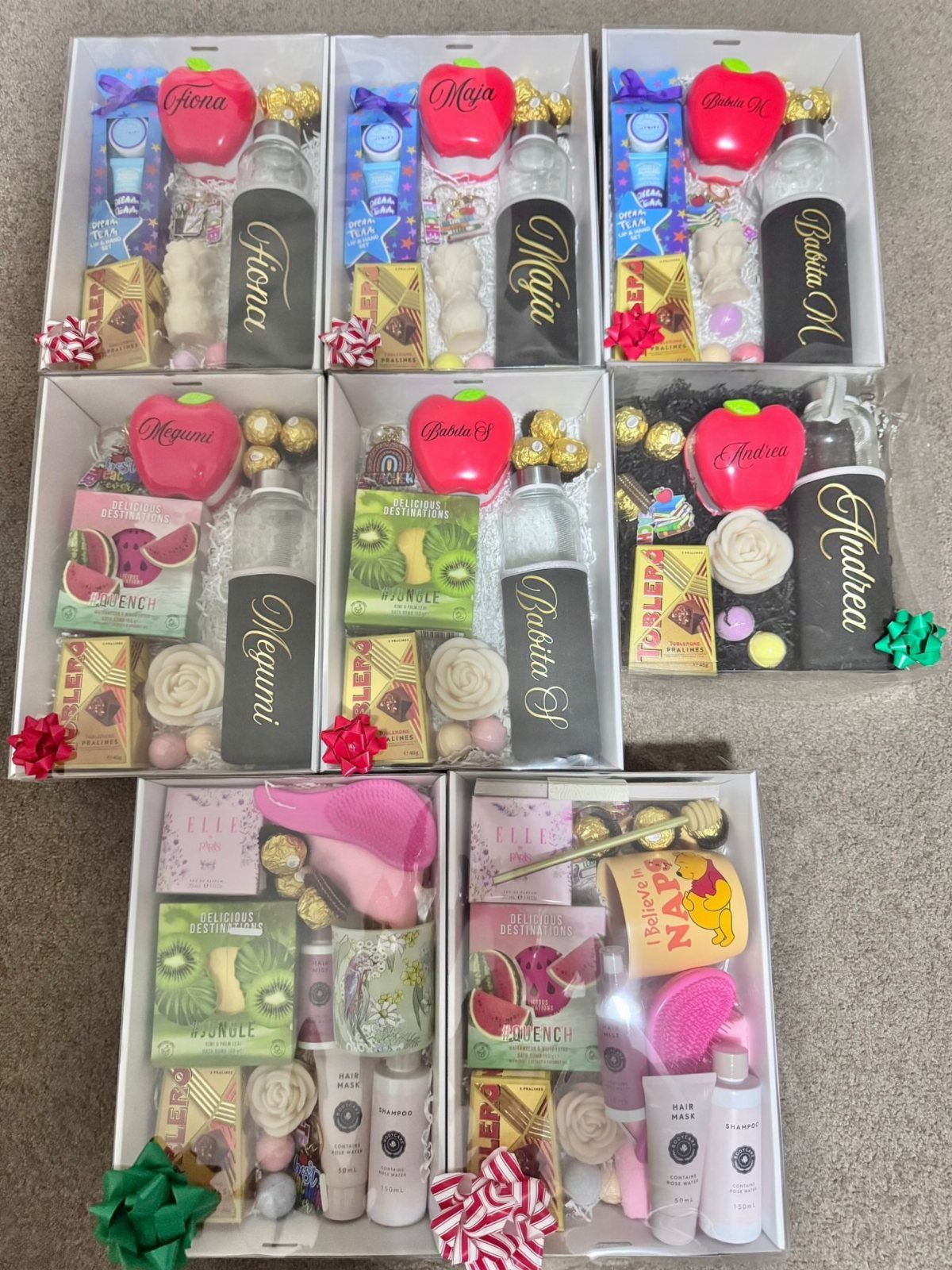 Seven white gift boxes containing personalized water bottles, apple accessories, and spa products.