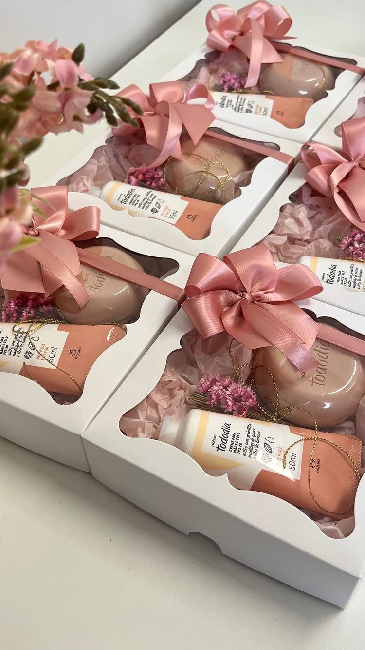 Pink skincare gift sets in white boxes tied with satin bows and flowers.
