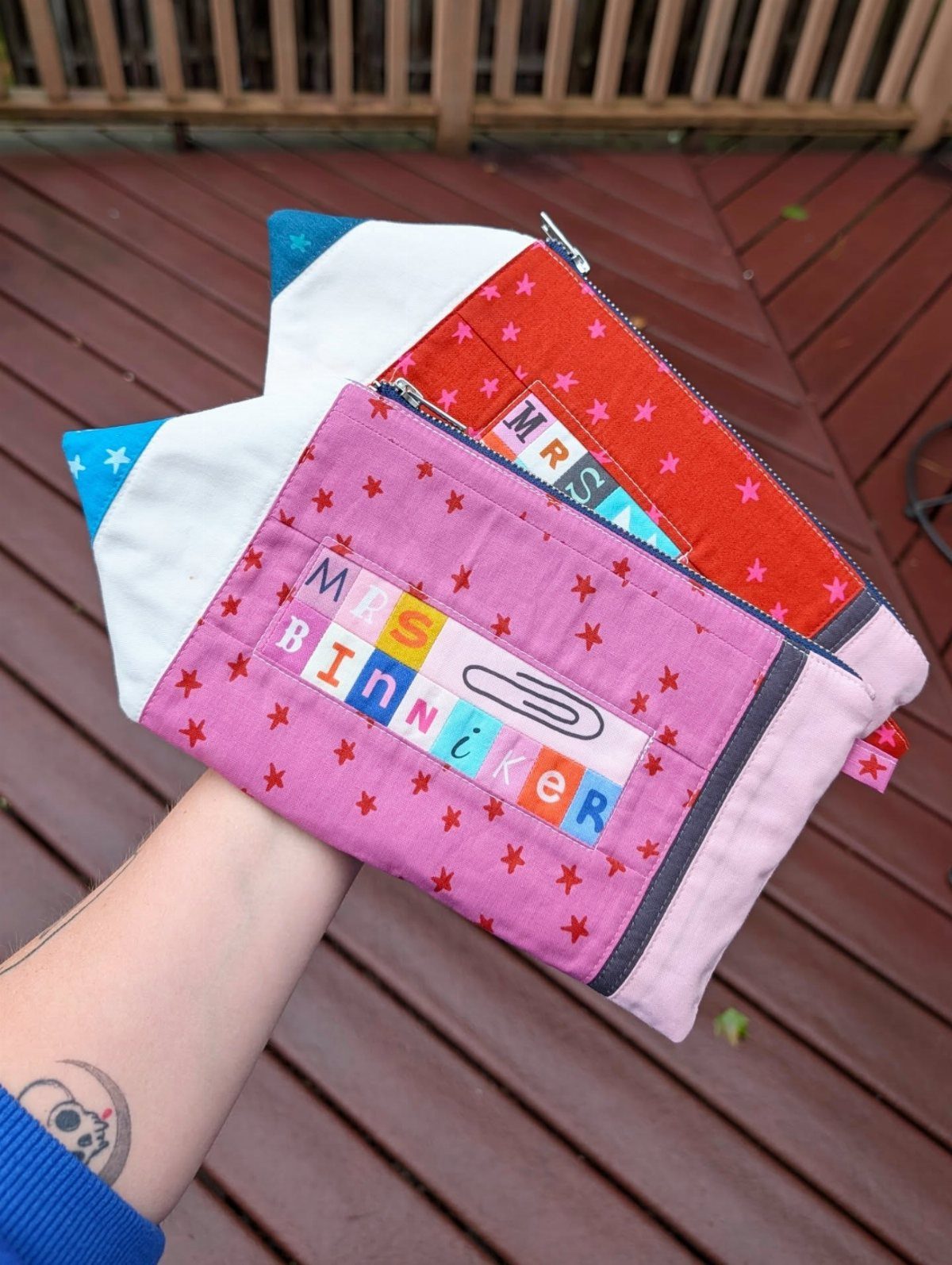 Personalized pink and red star-patterned fabric pouches held over a wooden deck.