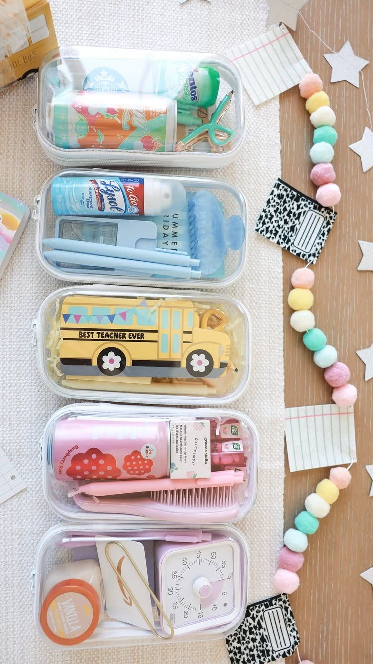 Five clear pouches filled with colorful school and personal care supplies and a pom-pom garland.