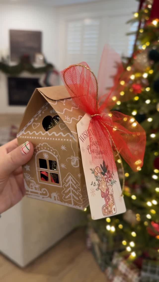 House-shaped brown gift box with red ribbon held in front of Christmas tree