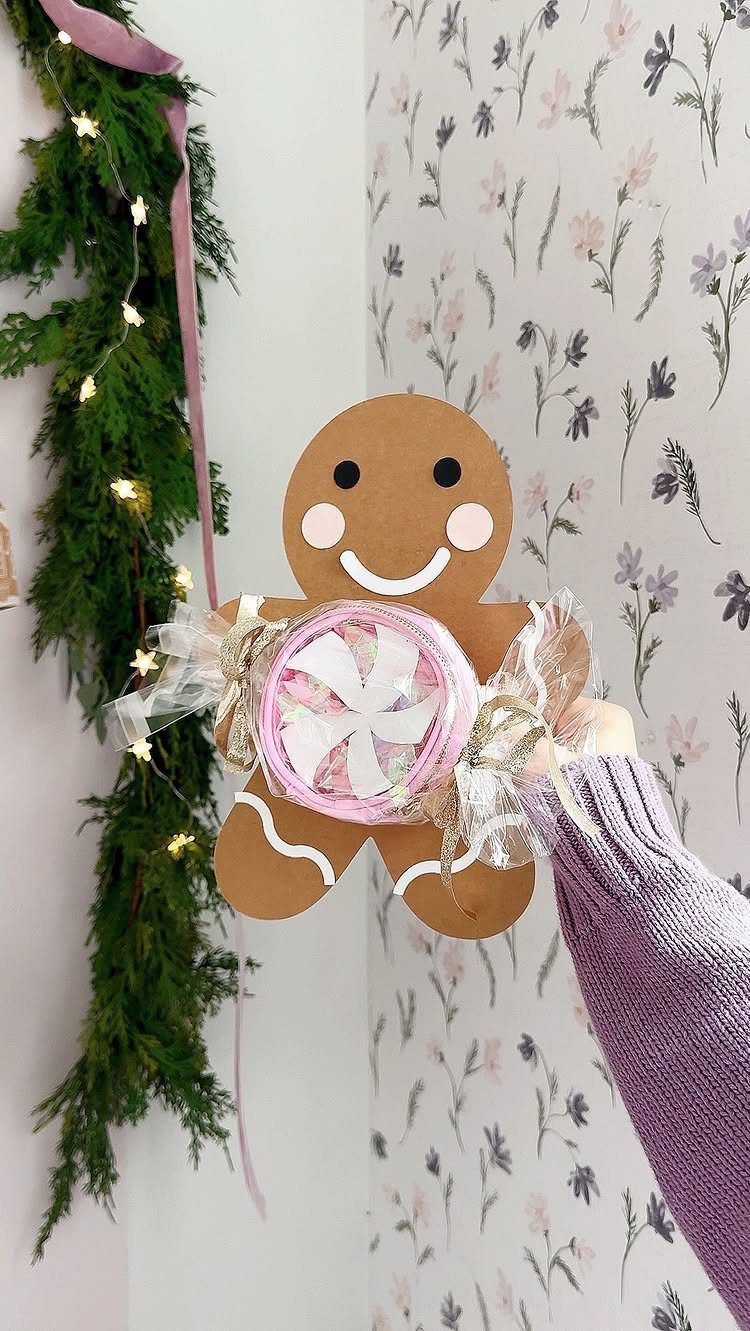 Cardboard gingerbread man holding a small pink wrapped gift against floral wallpaper