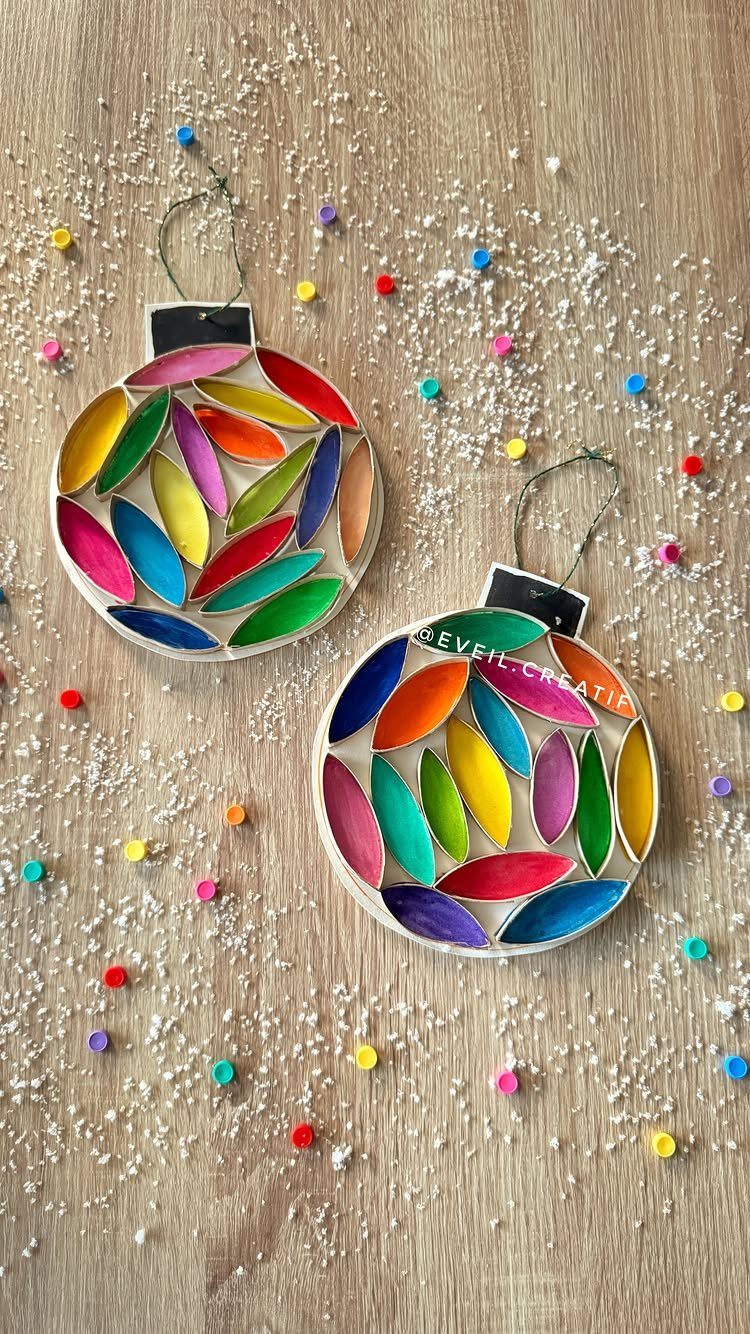 Two colorful handmade circular ornaments with leaf patterns on a snowy wooden surface.