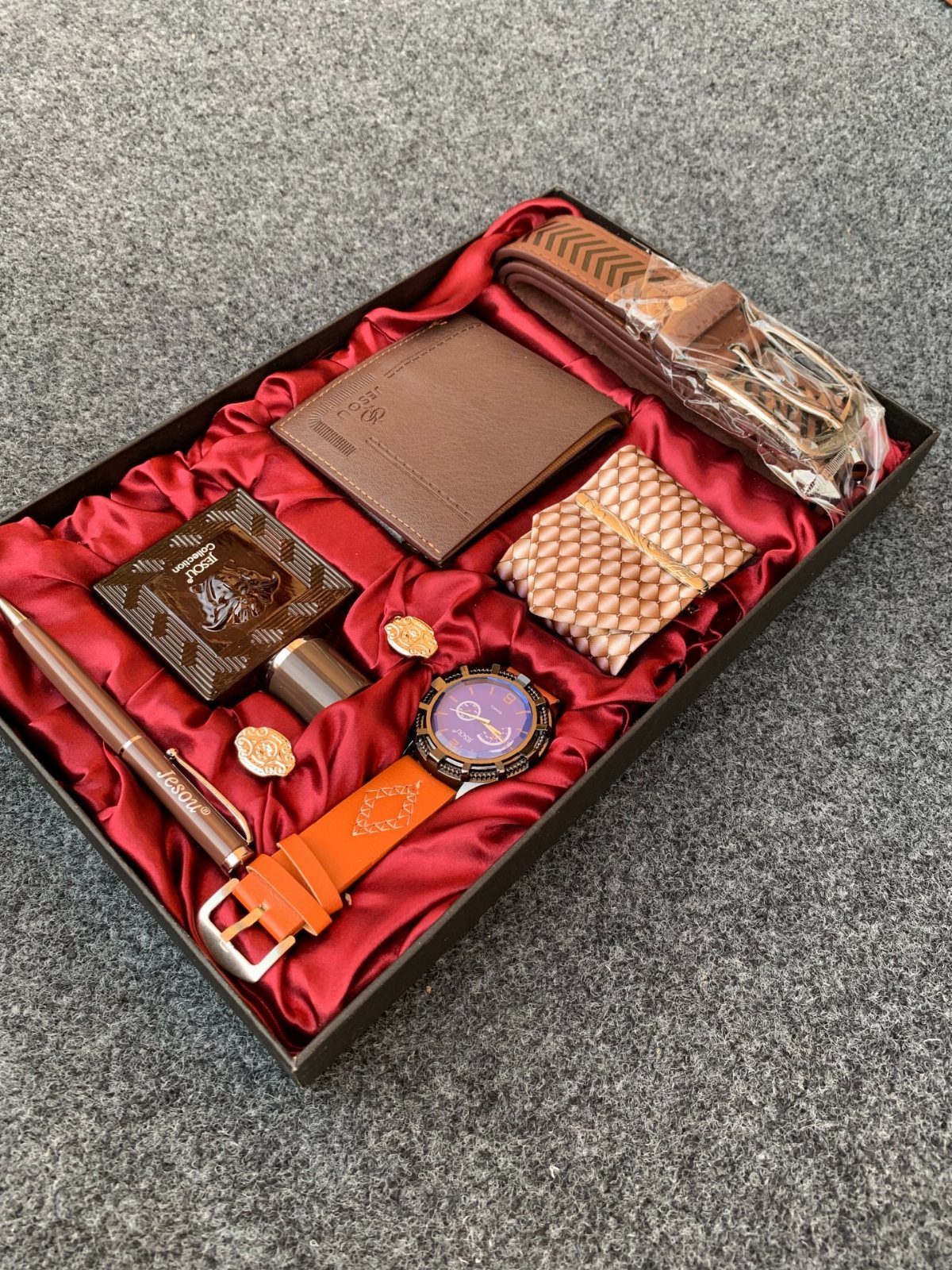 Brown leather wallet and accessories arranged in a red satin lined gift box.