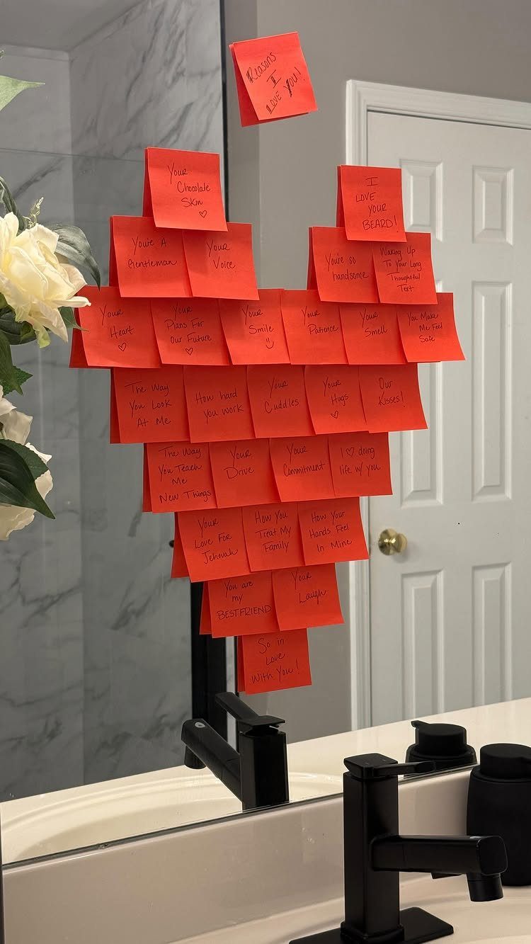 Red sticky notes arranged in a heart shape on a bathroom mirror.