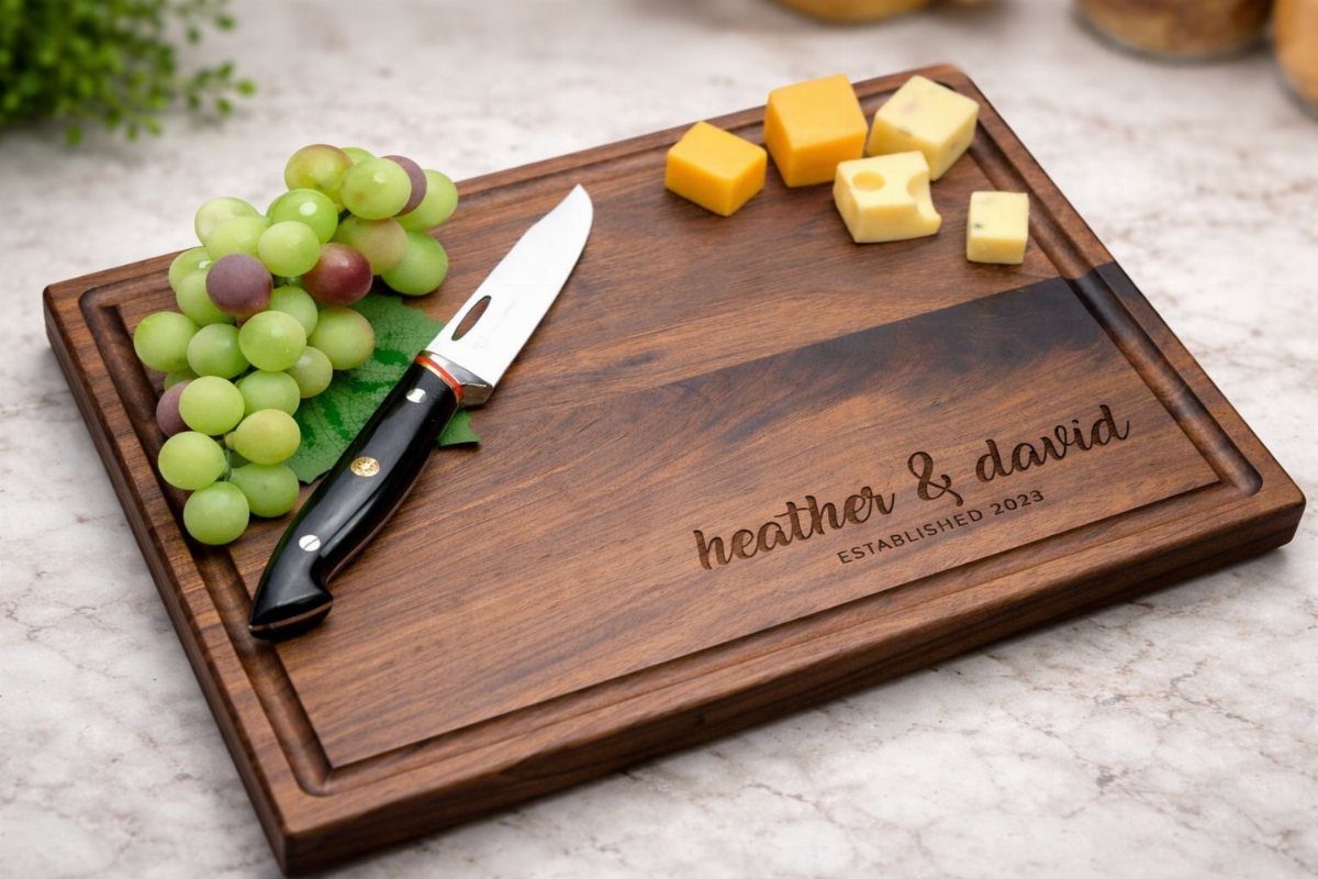 Personalized wooden cutting board with engraved names, cheese, grapes, and a knife.