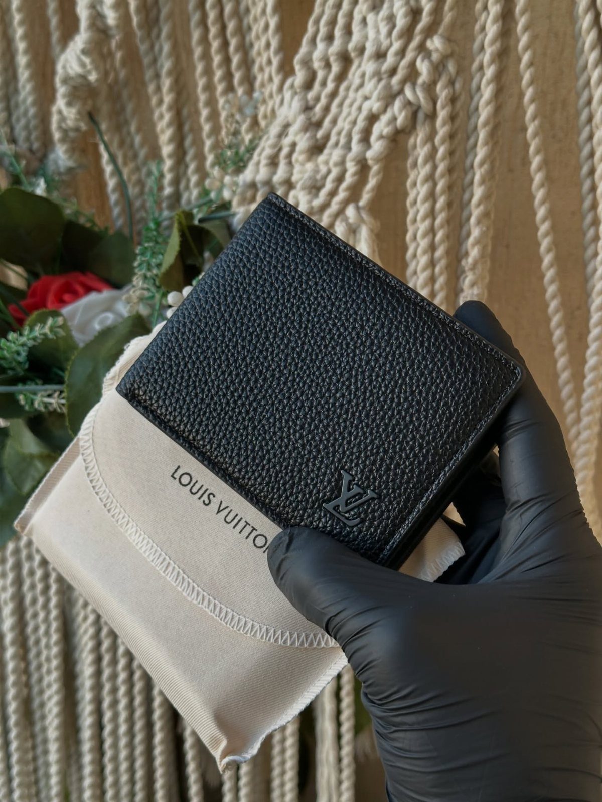 Black leather Louis Vuitton wallet held by a gloved hand against macrame background
