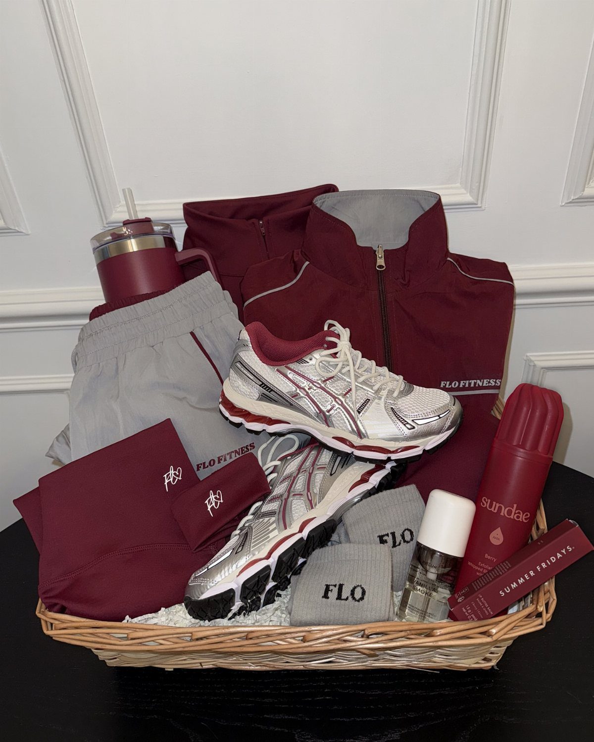 Athletic gift basket with maroon jacket, grey shorts, sneakers, and fitness accessories.