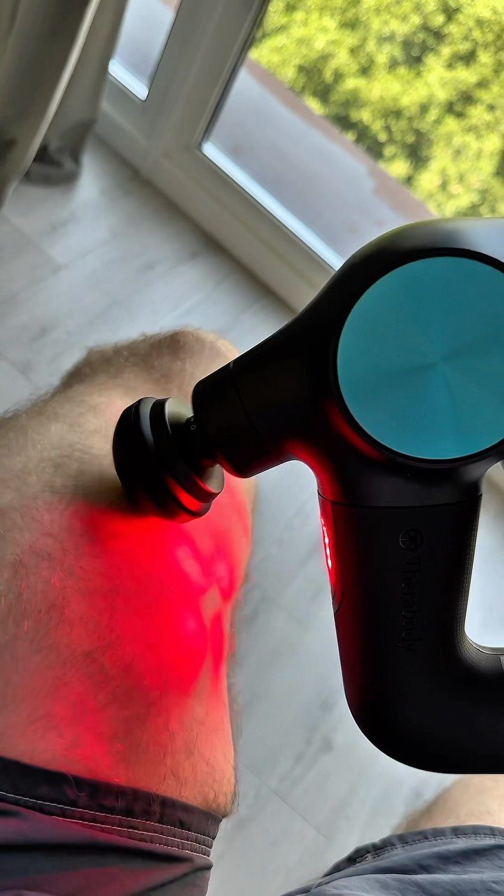Black massage gun with red light being used on a man's leg