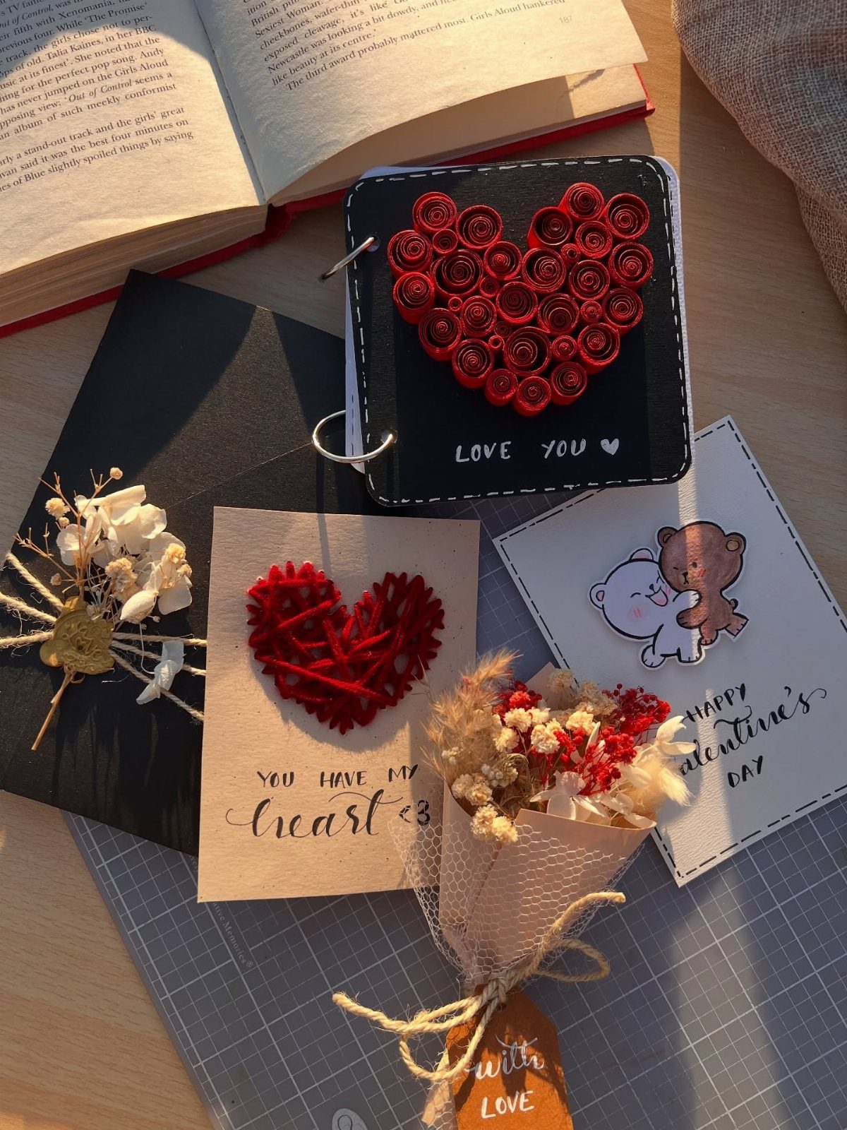 Handmade Valentine's Day gifts including a heart-decorated notebook, cards, and dried flowers.