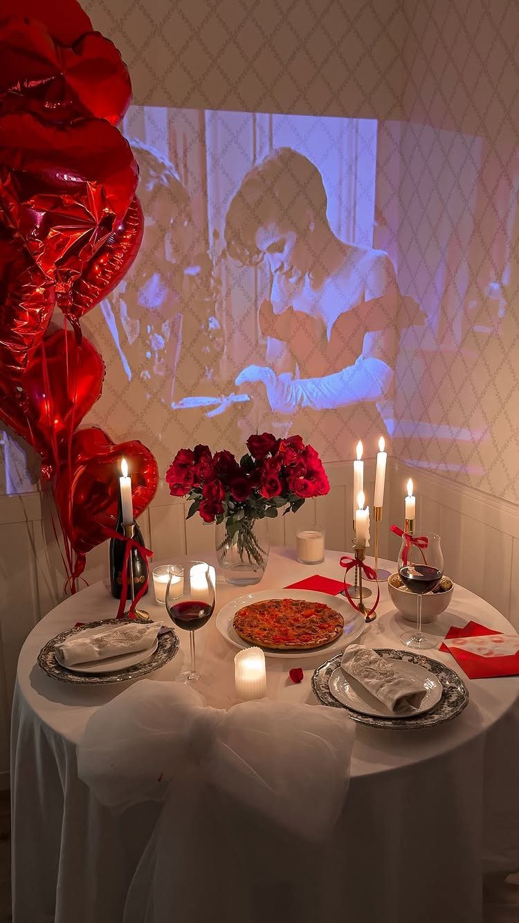 Romantic dinner table with red roses, candles, and a movie projected on the wall.