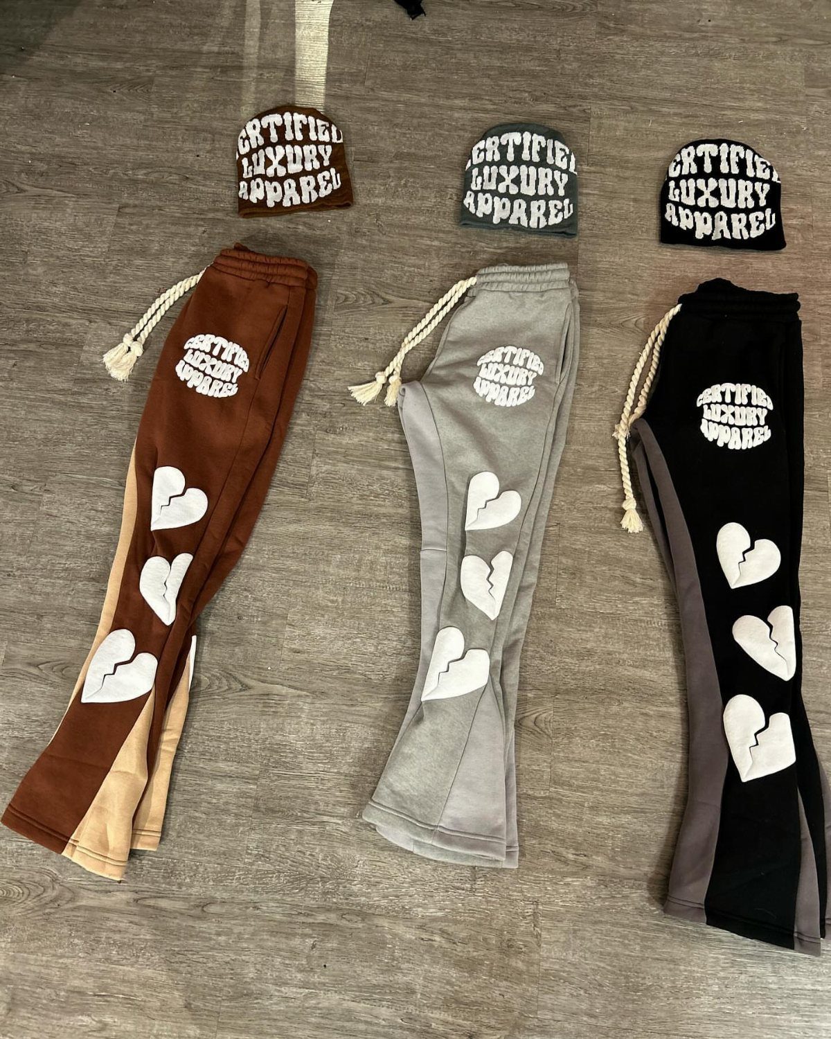 Three pairs of heart-patterned sweatpants and matching beanies in brown, grey, and black.