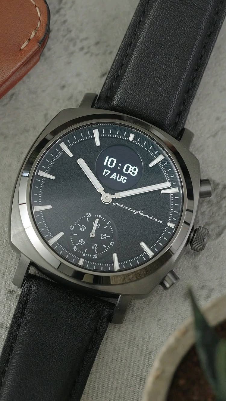 Black leather wristwatch with a dark face resting on a grey textured surface.