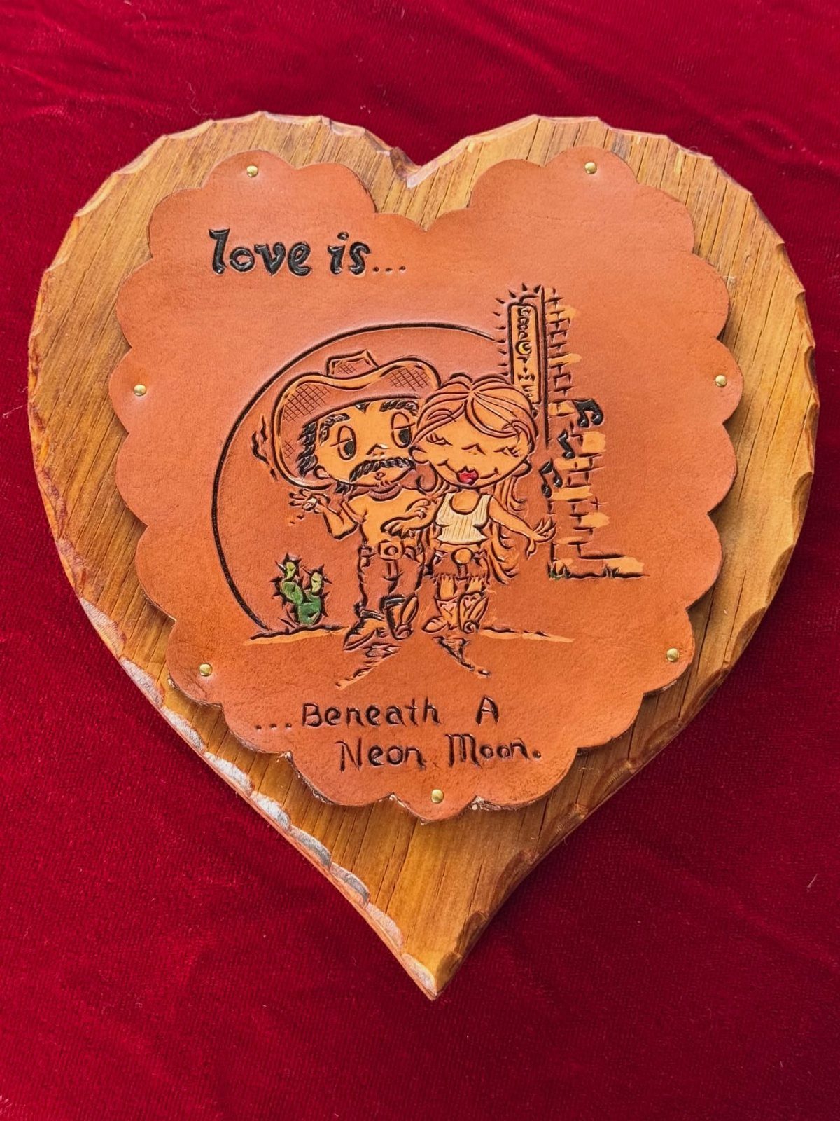 Heart-shaped wooden plaque with leather engraving of a cowboy and cowgirl couple.