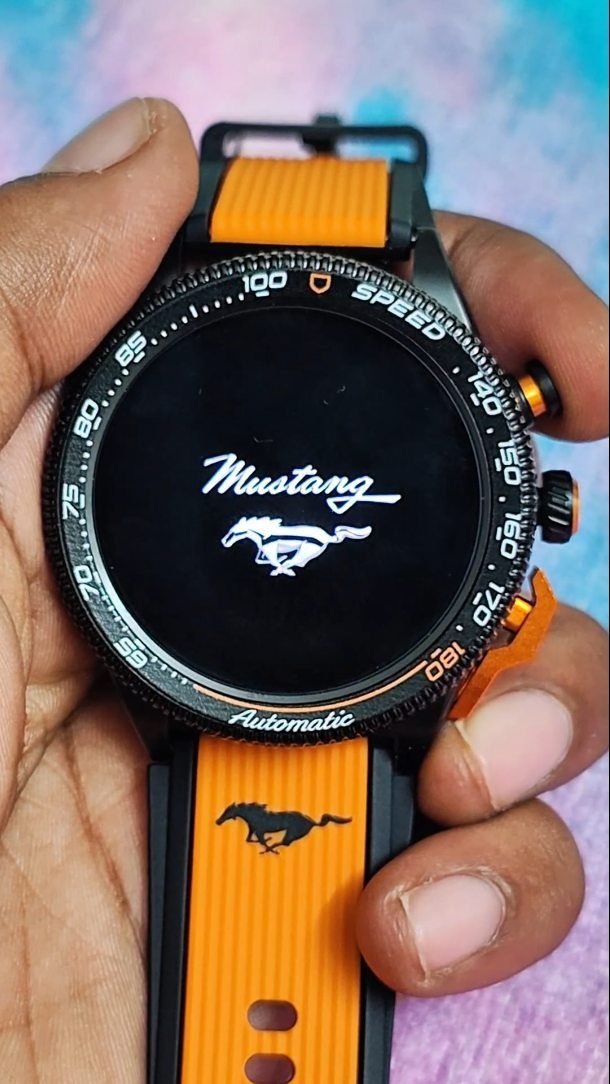 Black and orange Mustang smartwatch held in a person's hand against purple fabric