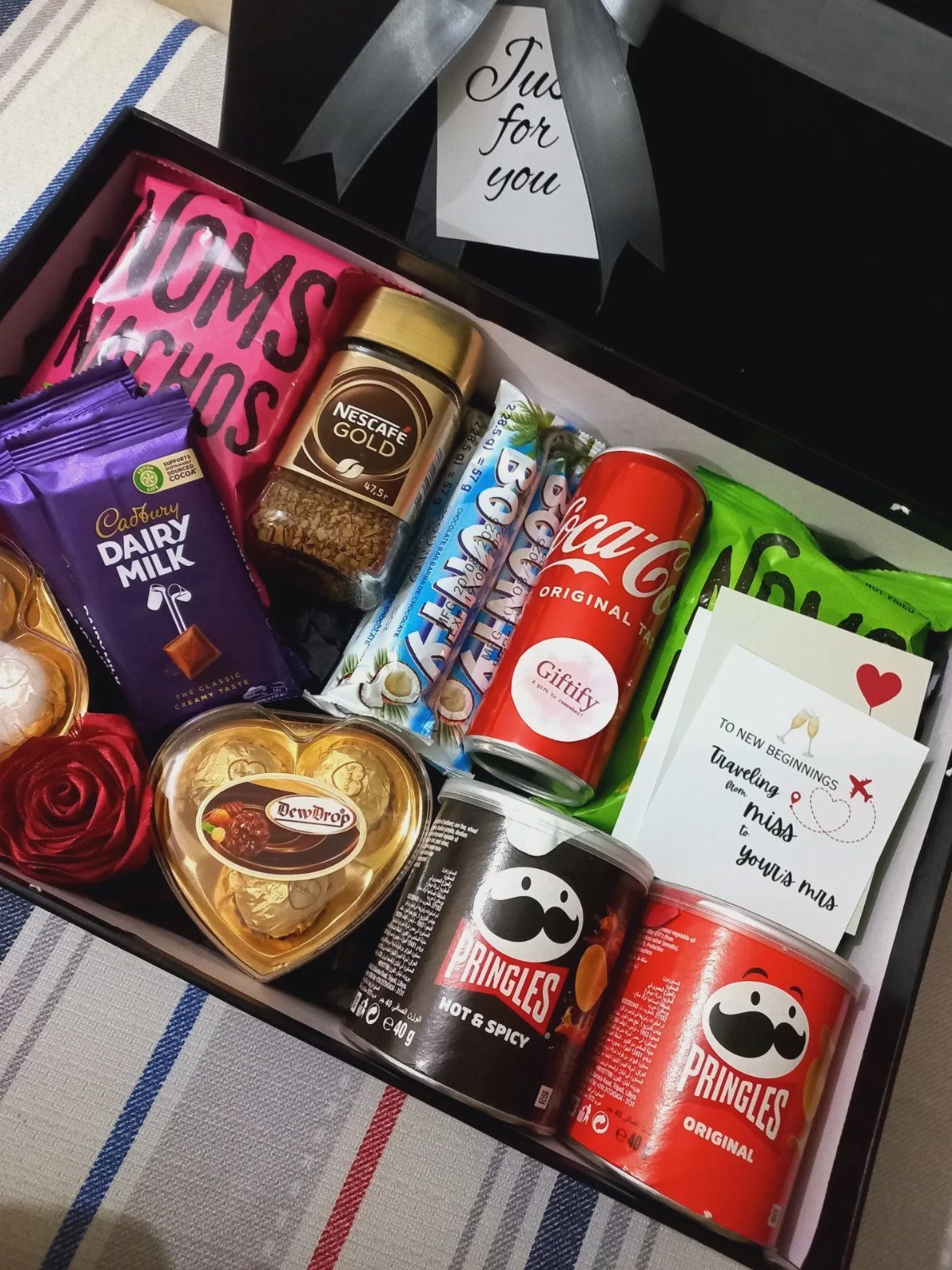 Gift box for men containing snacks, drinks, chocolates, and a red rose.