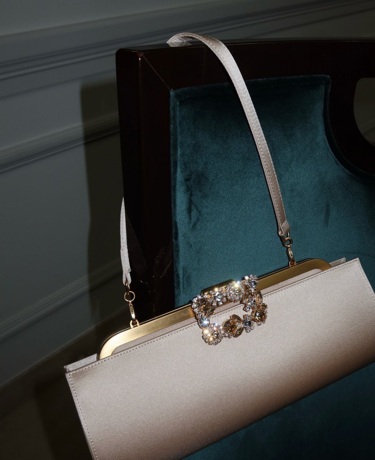Champagne satin structured clutch bag with jeweled clasp on a teal velvet chair