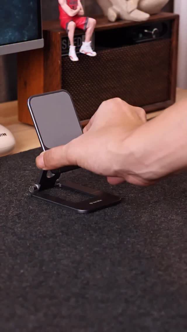 Hand adjusting a smartphone on a black metal stand on a desk mat
