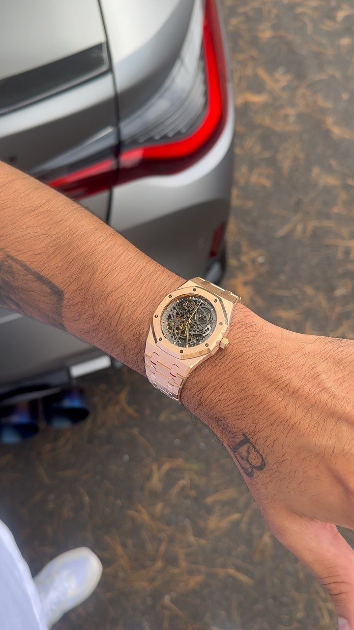 Gold luxury watch with skeleton dial worn on a tattooed wrist by a car