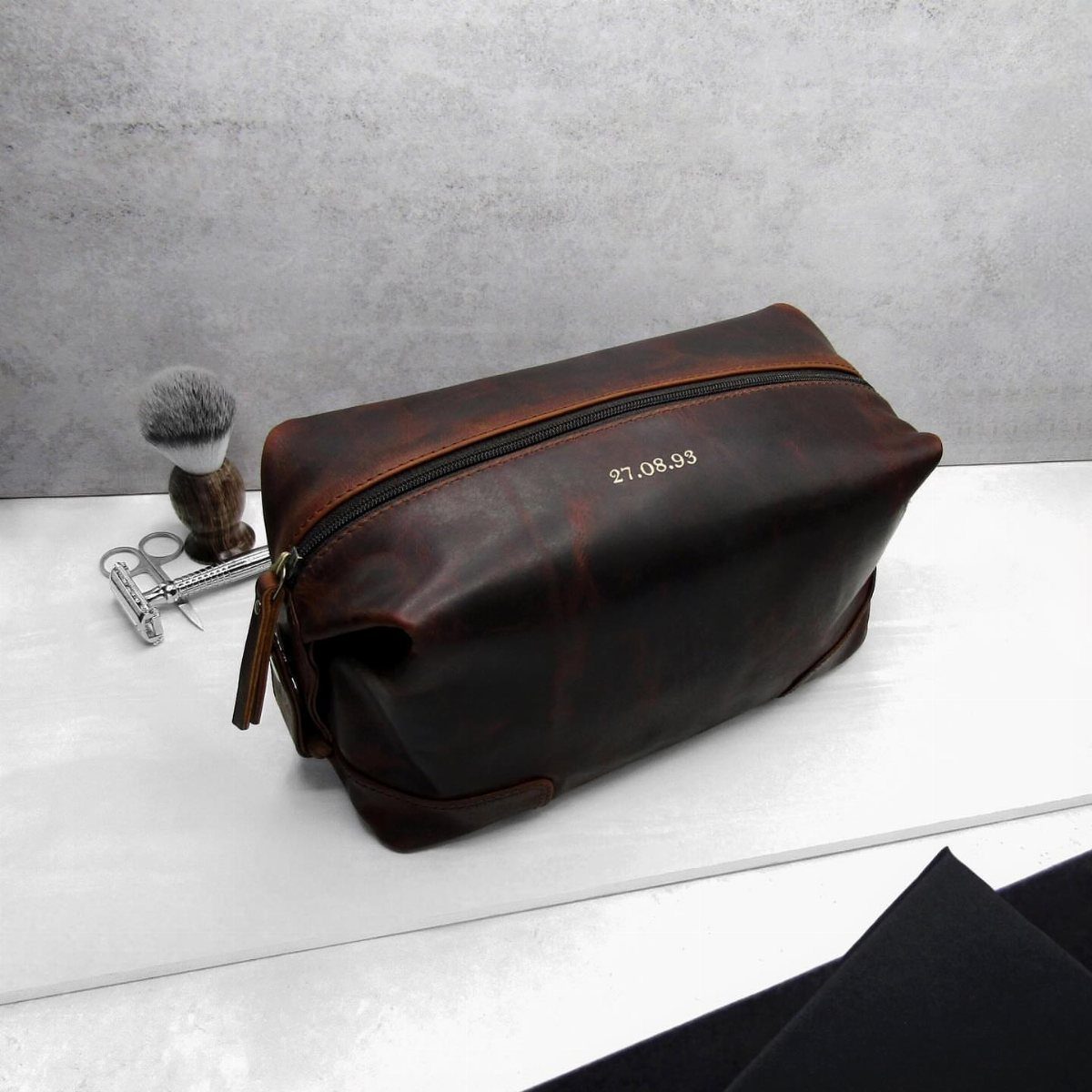 Brown leather toiletry bag with embossed date next to grooming tools