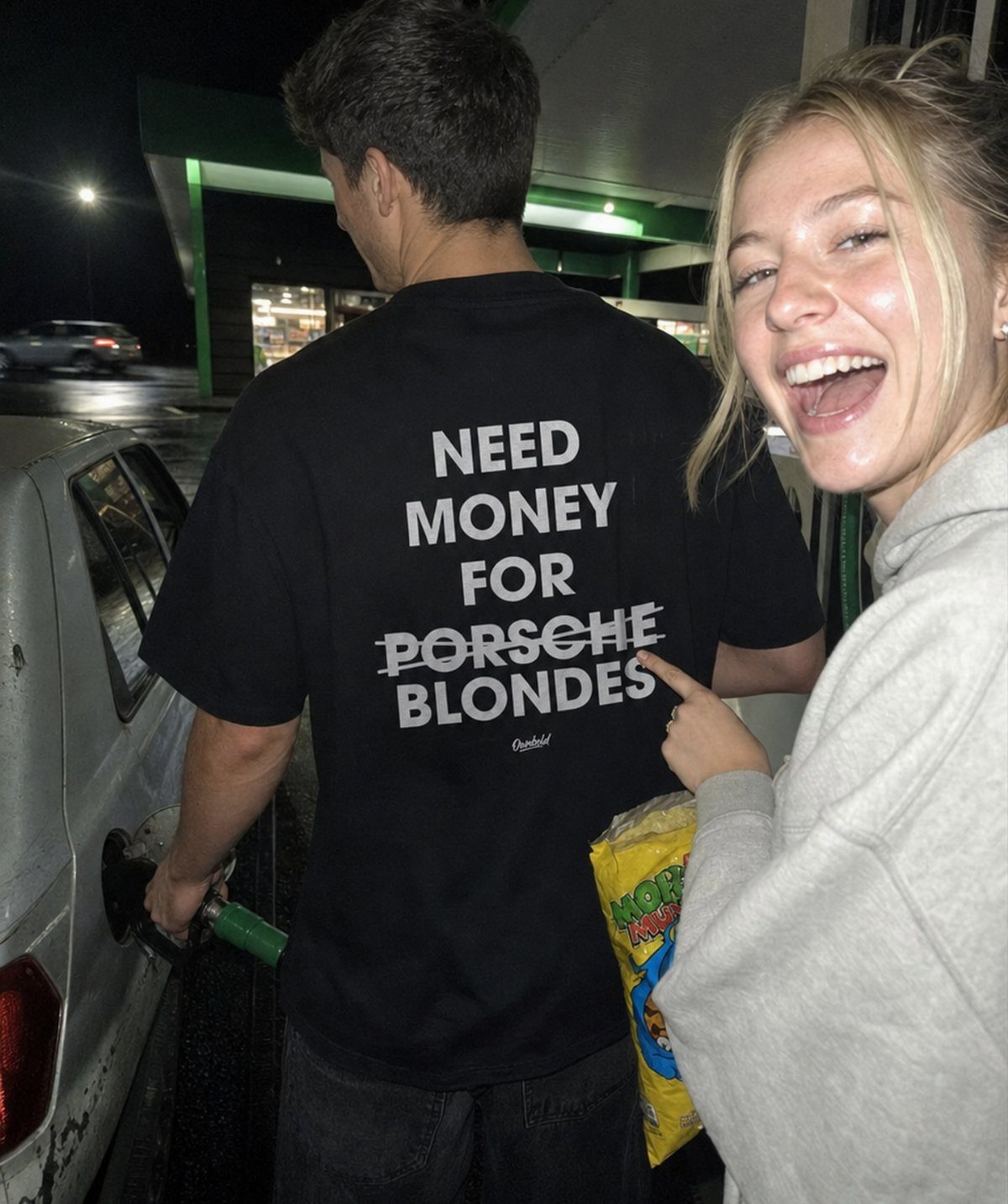 Man wearing a black printed t-shirt with white text at a gas station.