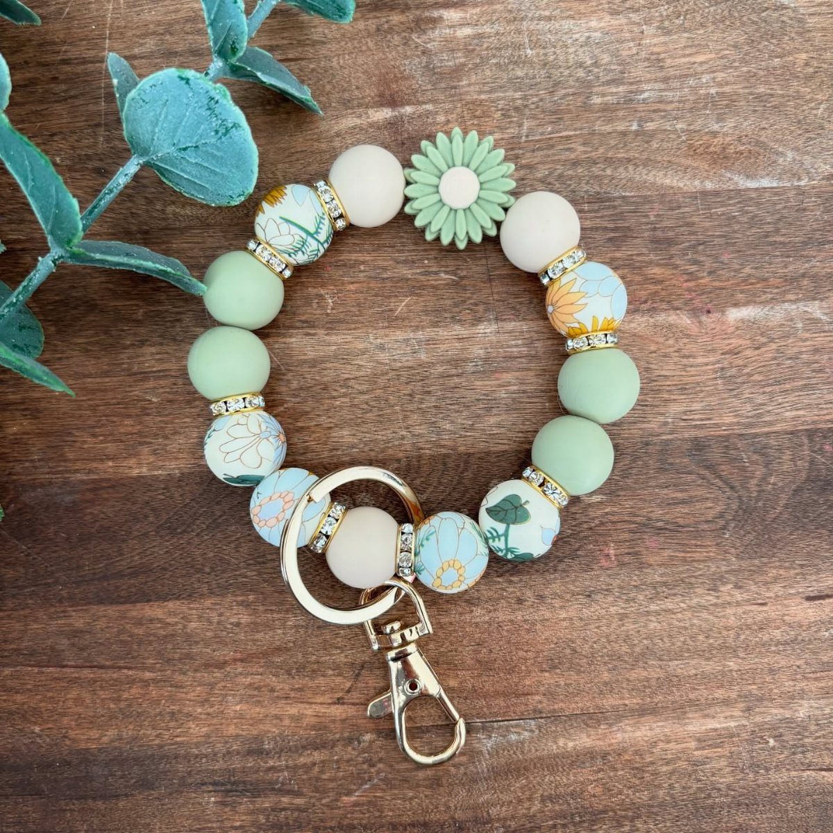 Beaded wristlet keychain with floral patterns and a daisy on wooden background