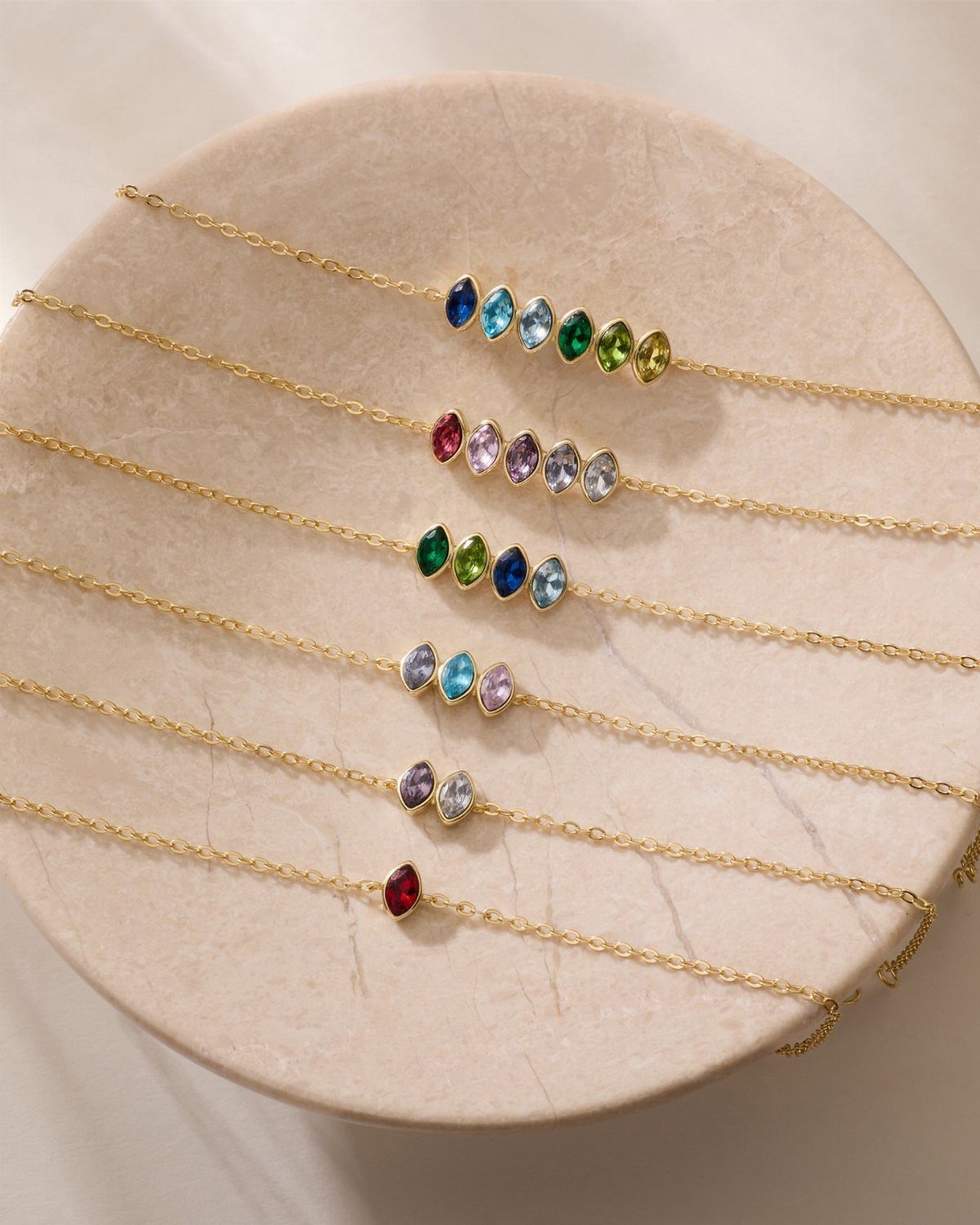 Gold necklaces with colorful gemstones resting on a round beige stone platter.
